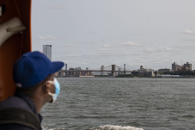 A man wearing a PPE mask takes in the view of The Brooklyn Bridge as he rides The Staten Island Ferry into NYC in Manhattan, New York.